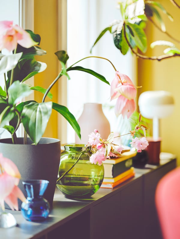 Green plants and cut flowers poke out of KONSTFULL glass vase and PERSILLADE plant pot, on top of cabinets.