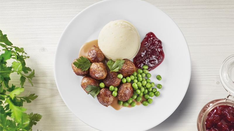 Ein weißer Teller mit Fleisch(los)bällchen, Kartoffelpürre, Erbsen und Preiselbeeren.