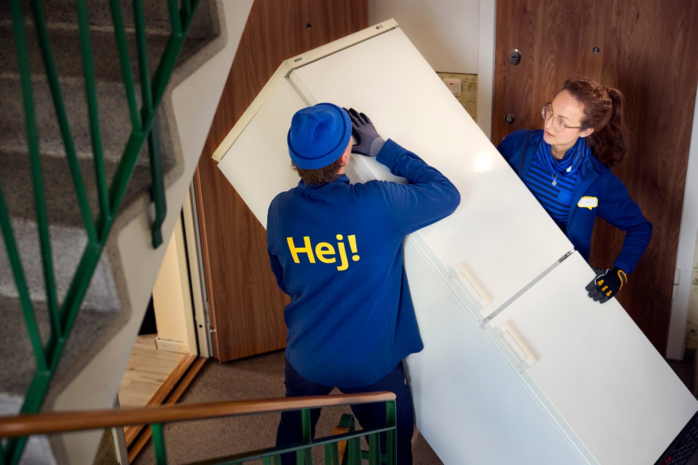 Dwoje pracowników IKEA znosi lodówkę po schodach.