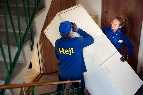 Kobieta i mężczyzna wynoszą starą lodówkę z mieszkania