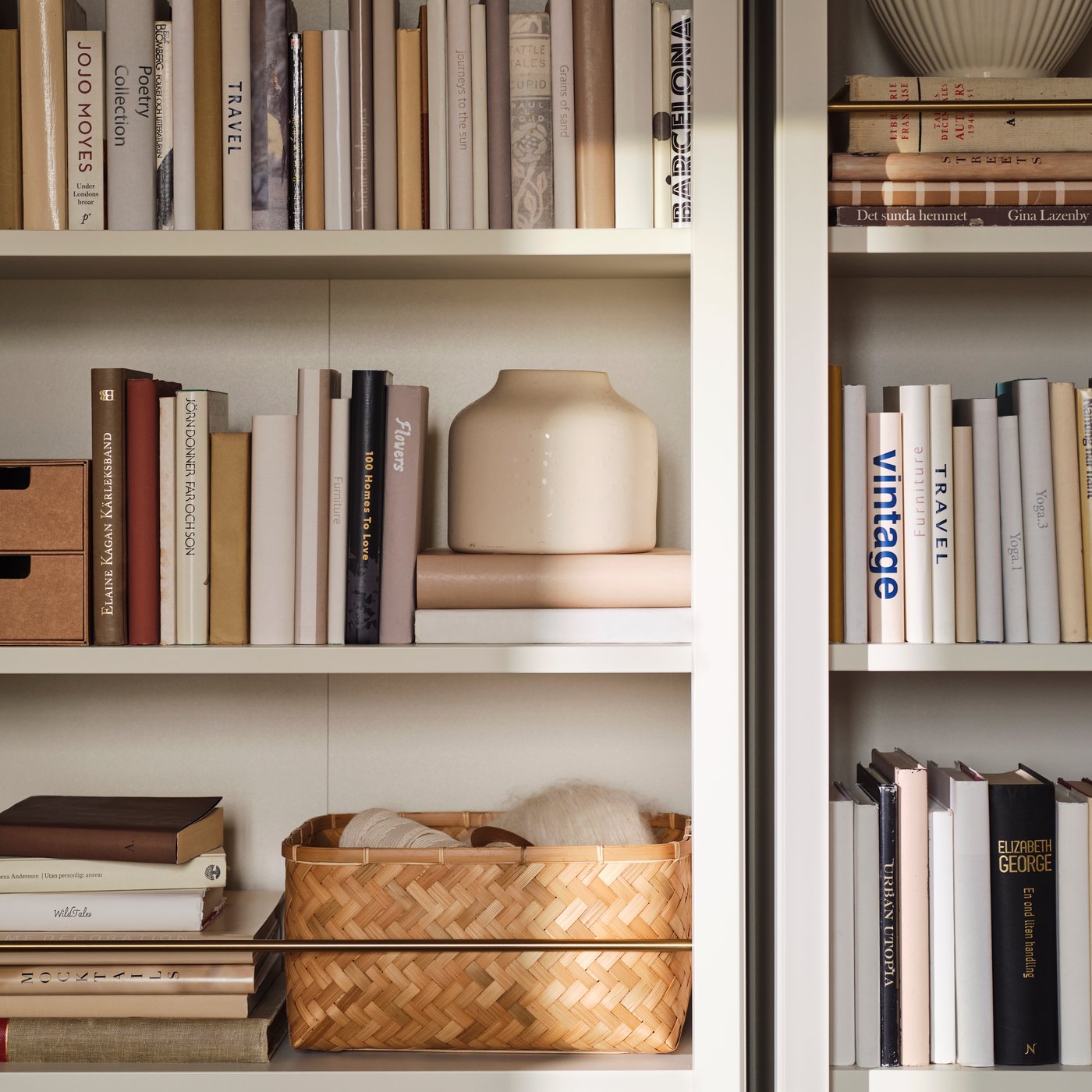 Zbliżenie na kremowy regał FÄRJKARL wypełniony książkami, dekoracjami i koszykami.