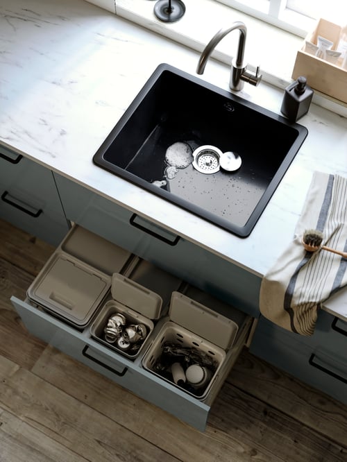 Blick von oben auf eine KILSVIKEN Einbauspüle in einer EKBACKEN Maßarbeitsplatte. Darunter sind in einer geöffneten Schublade HÅLLBAR Behälter mit Deckel zu sehen, in denen Recyclinggut gesammelt wird.