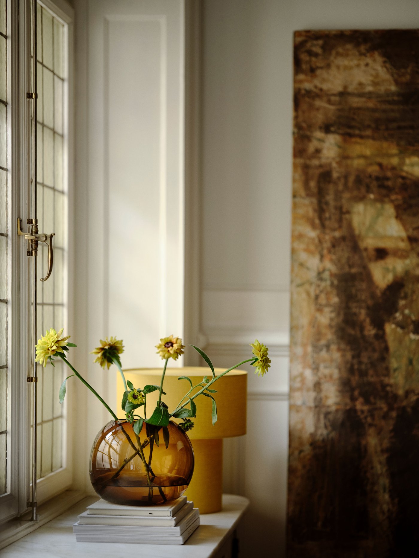 مزهرية زجاجية بنية اللون منفوخة يدوياً تحمل اسم "ستوكهولم 2025" ومصباح طاولة أصفر اللون مزود بنافذة من المجموعة.