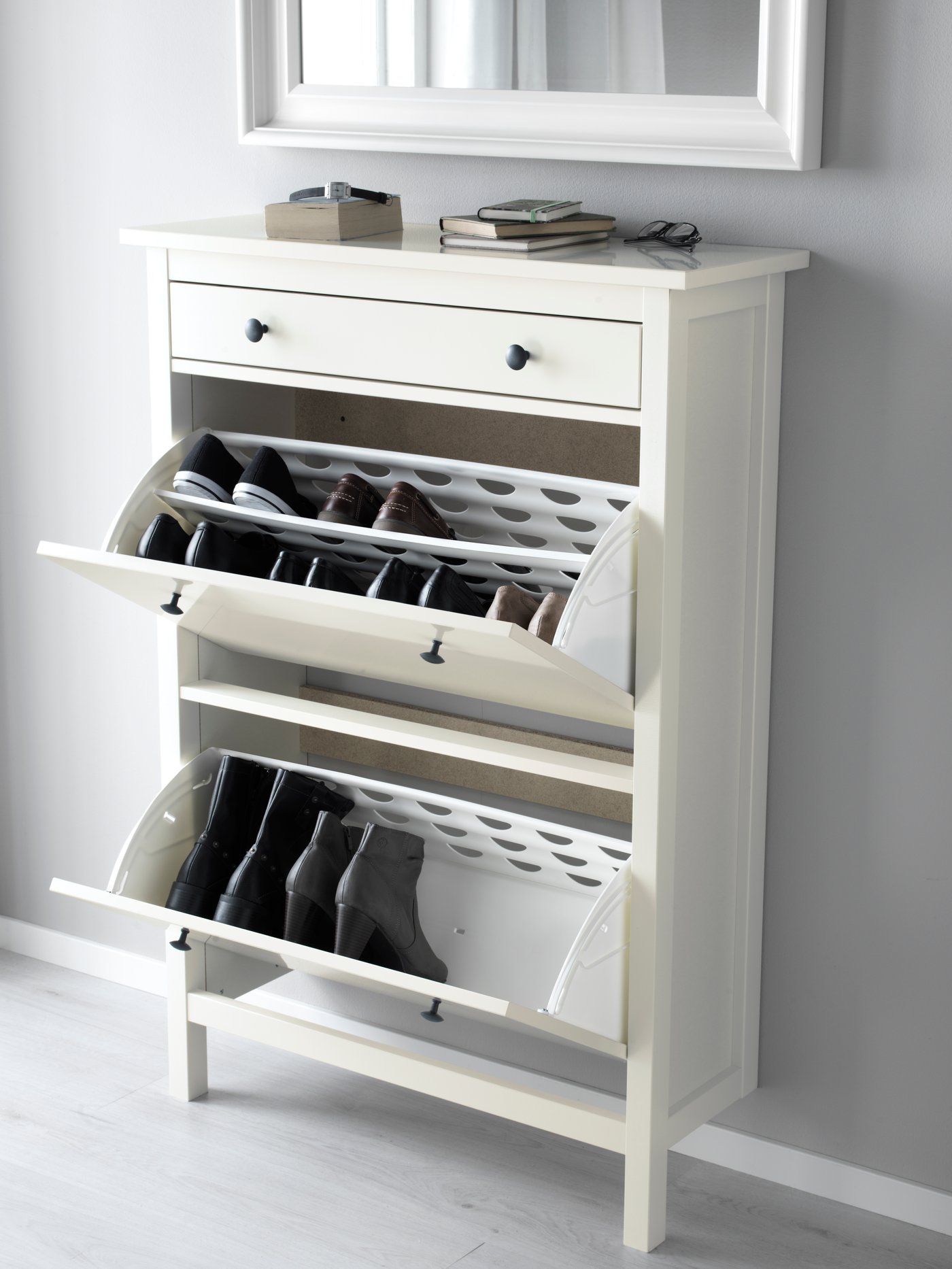 Un zapatero HEMNES blanco apoyado a una pared con sus cajones abiertos mostrando zapatos.