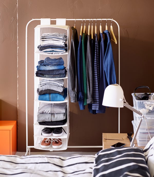 A clothing rack with a white SKUBB storage with 6 compartments and clothing hanging on hangers.