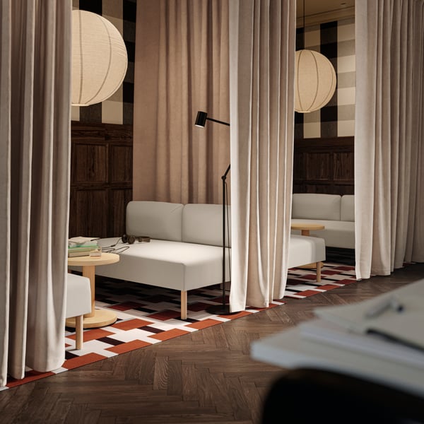 A break room with four beige/wood LILLEHEM sofas, two geometric rugs, and beige SANELA curtains closing off the space.