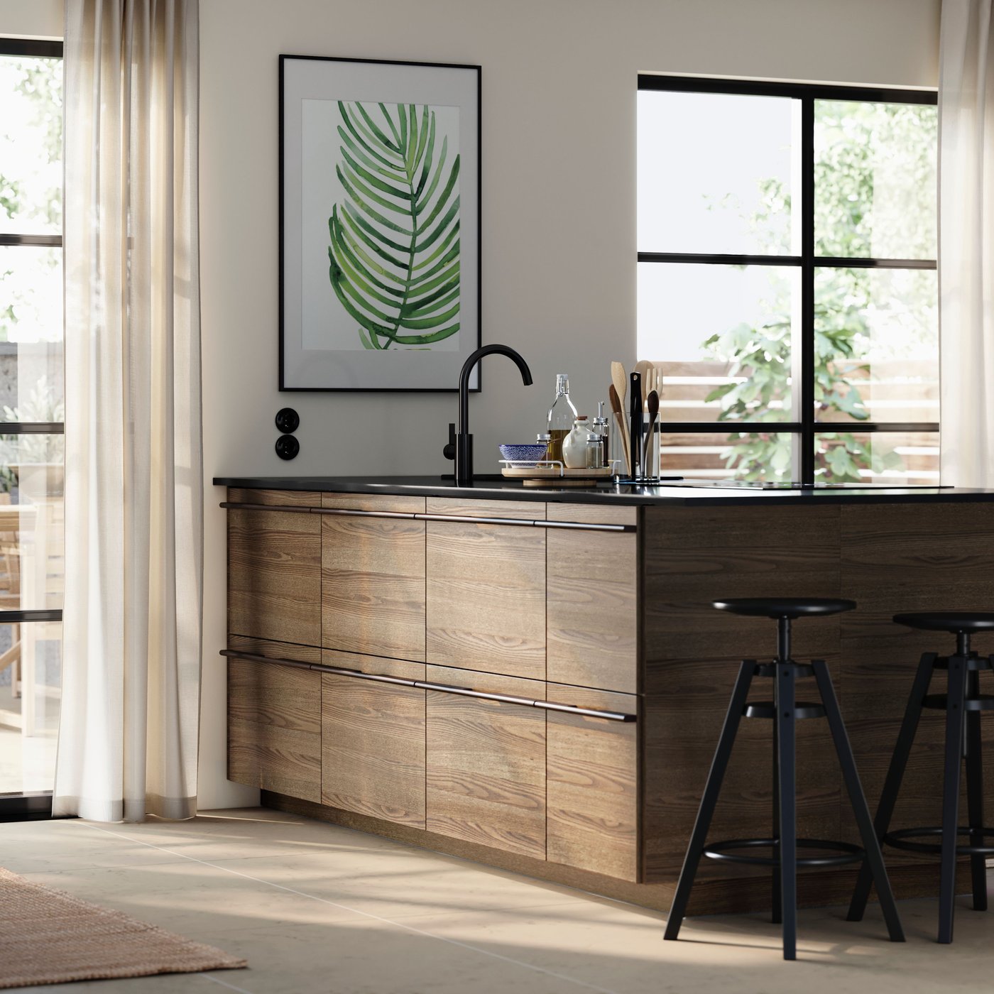 Wyspa kuchenna z frontami STENSTA z ciemnobrązowym fornirem jesionowym, stołki barowe i duży plakat z liściem na ścianie.