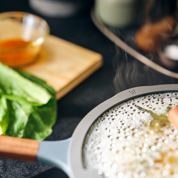A KLIPPFISK sauté pan on a stovetop with steam rising from under the lid.