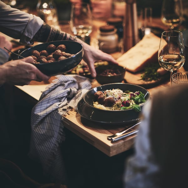 Un invité assis à une longue table passant un bol de boulettes végétales HUVUDROLL à une autre personne assise à ses côtés.