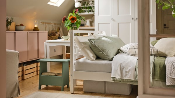 A rustic-style bedroom contains a HAUGA extendable table by a white TARVA bed covered in green/stripe BERGPALM comforter set.