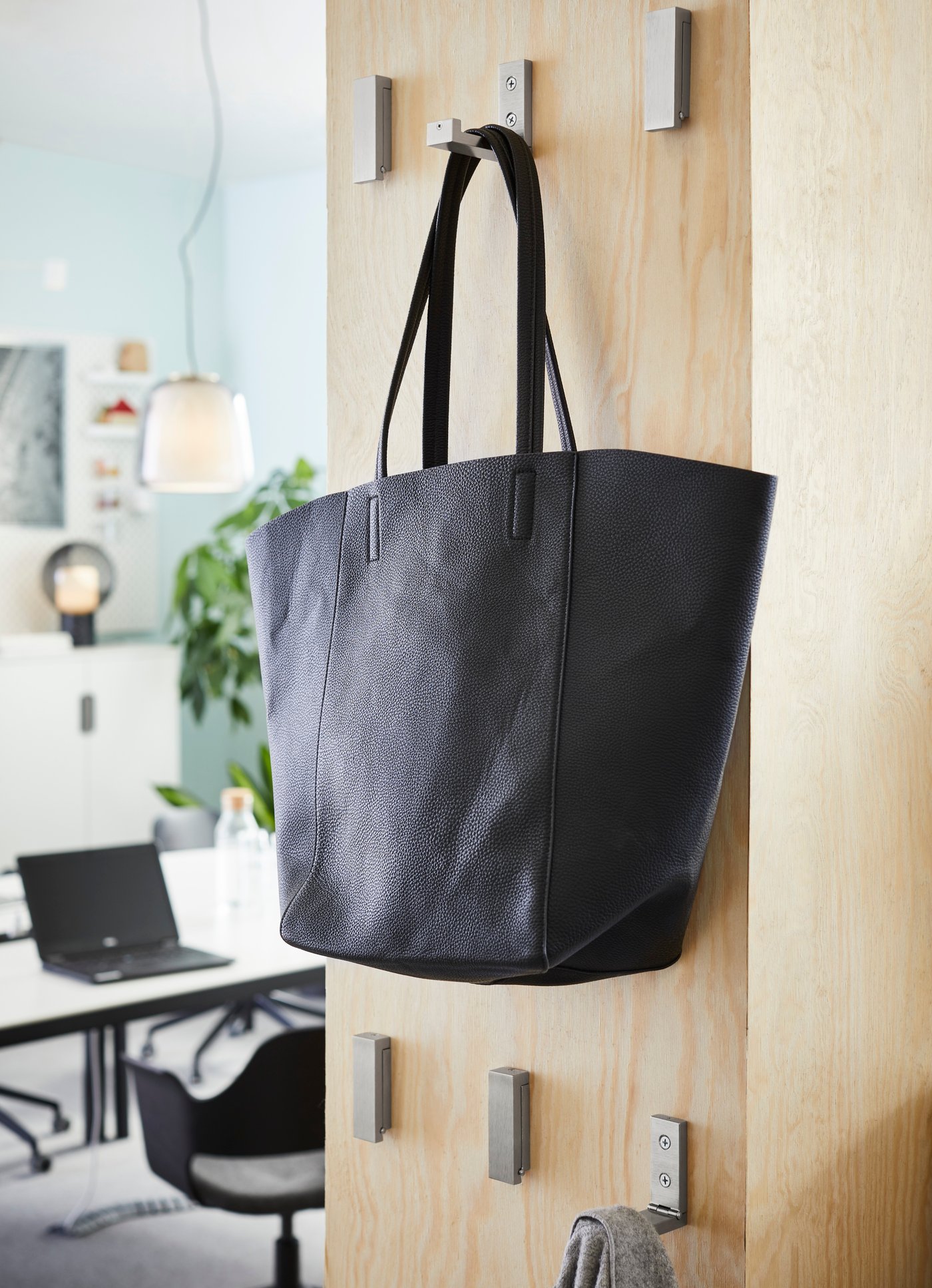 BJÄRNUM aluminium folding hooks mounted to a partition wall, with a black tote hanging on one hook.