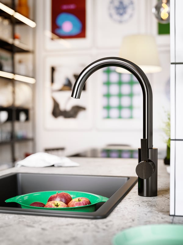 A black quartz composite insert sink and a brushed black metal kitchen mixer tap on a limestone effect/laminate worktop.