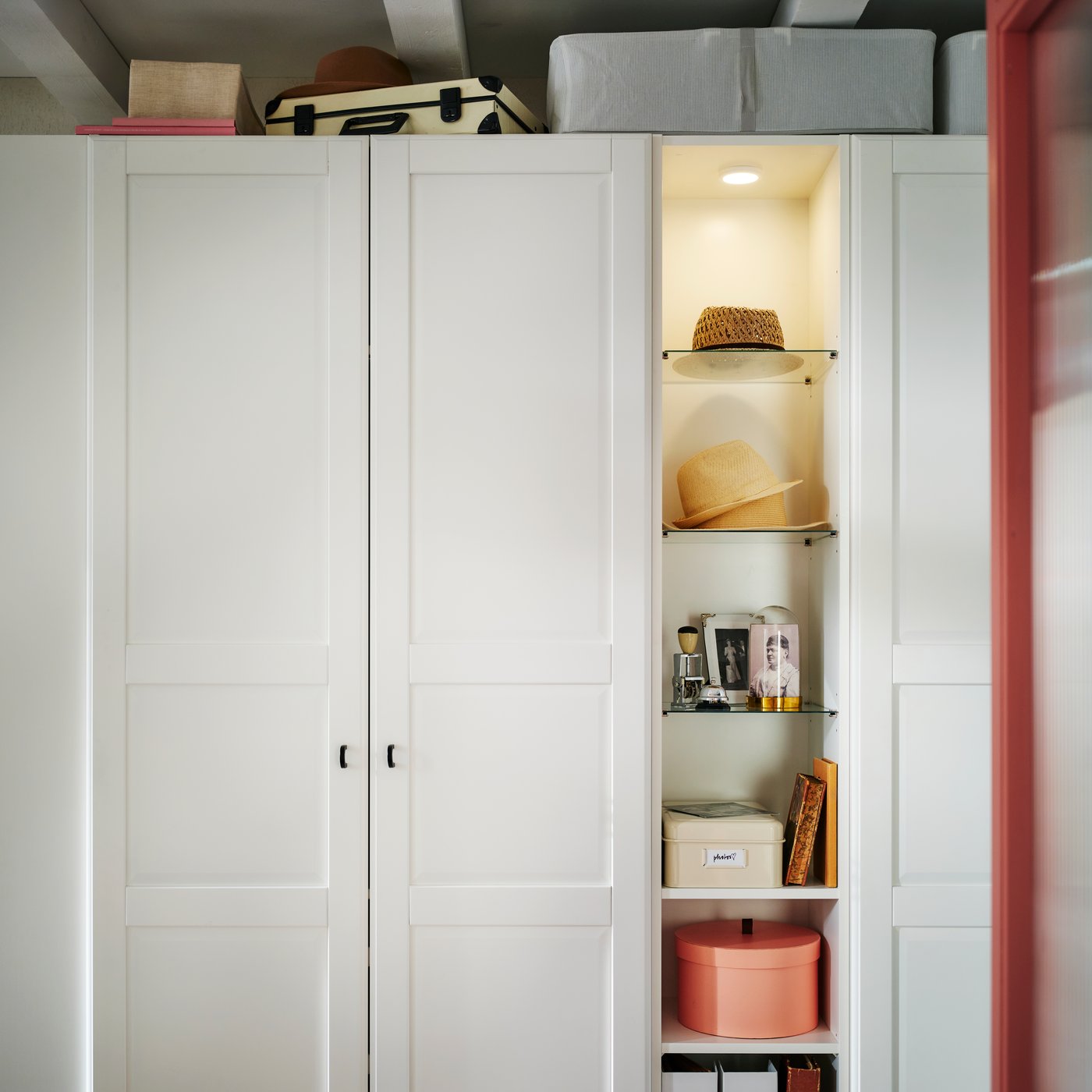 A white PAX/TYSSEDAL wardrobe with mid-unit has hats, knick-knacks and boxes on the shelves and larger storage boxes on top.