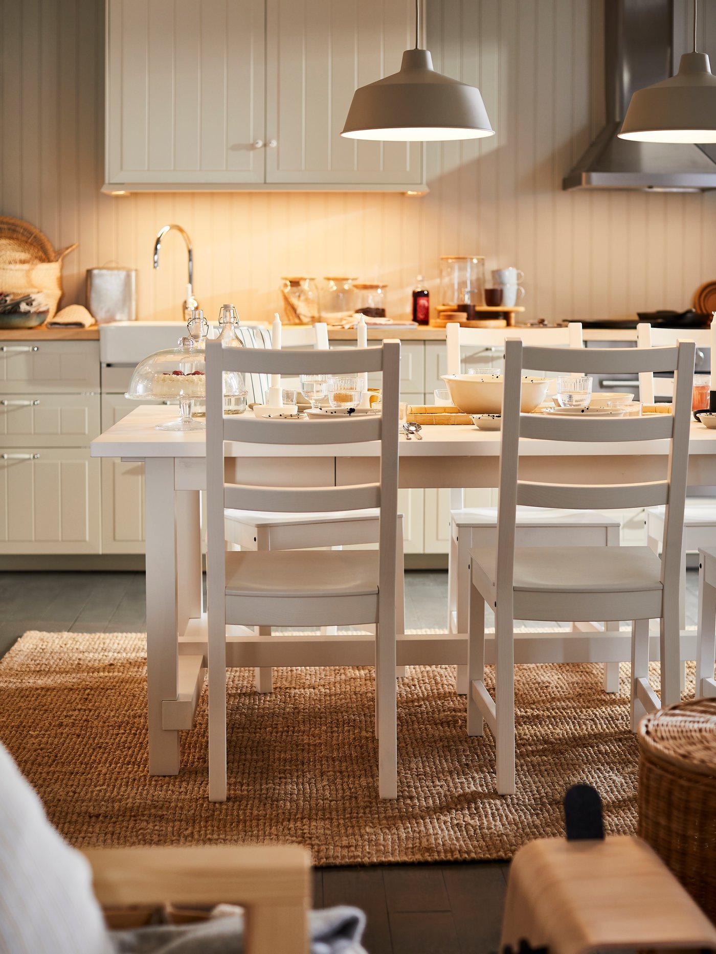 Ein weißer langer Tisch mit weißen Stühlen steht vor einer weißen Küchenzeile.