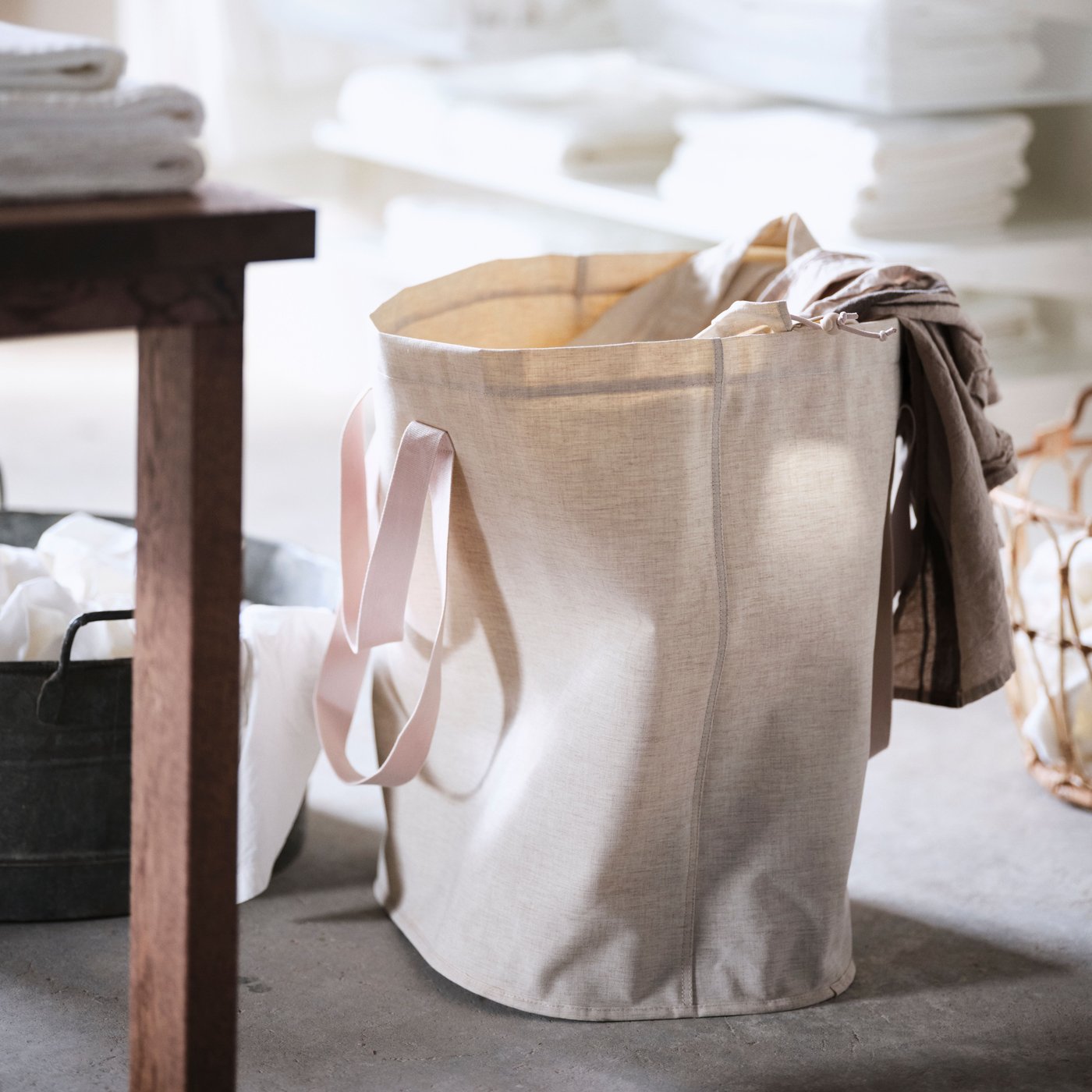 A half full PURRPINGLA laundry bag standing on the floor next to a brown wooden table.