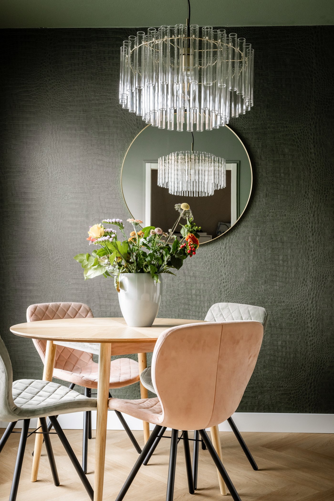Eetkamerhoek met ronde eettafel en vier stoelen in zachtroze en lichtgrijs. Boven de tafel hangt een STOCKHOLM 2025 lamp.
