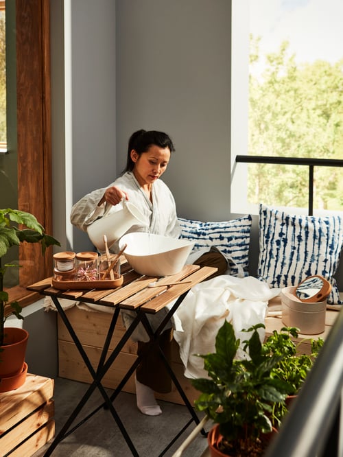 Outdoor area with table, bench, cushion covers, throw, box with mirror lid, jars with lids, vase, serving bowl, plant pots.