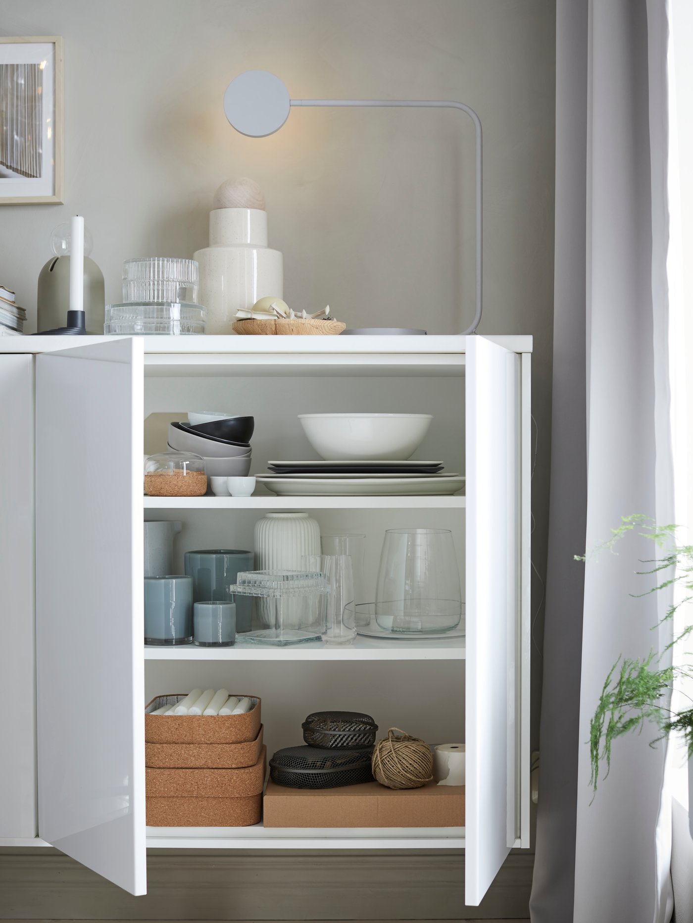 Een open, smalle uittrekbare kast met snijplanken op de onderste plank en oliën en kruiden op de bovenste.