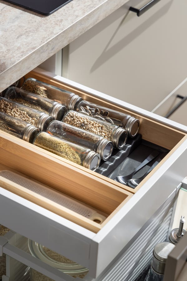 Close up of an open white kitchen drawer with wooden separators and various jars.