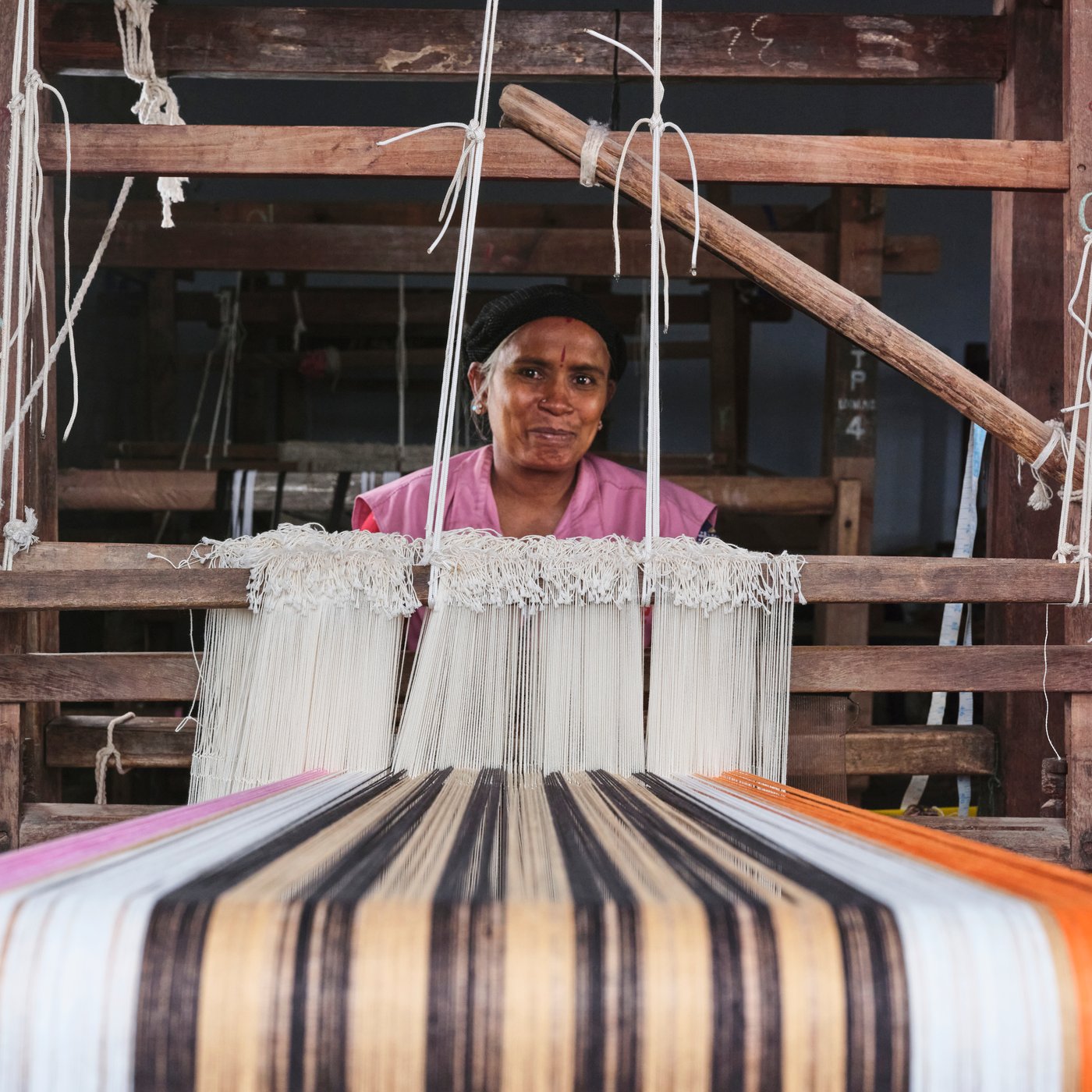 A person is sitting at a loom weaving a MÄVINN table-runner out of banana bark fibres and cotton threads in vibrant colours.