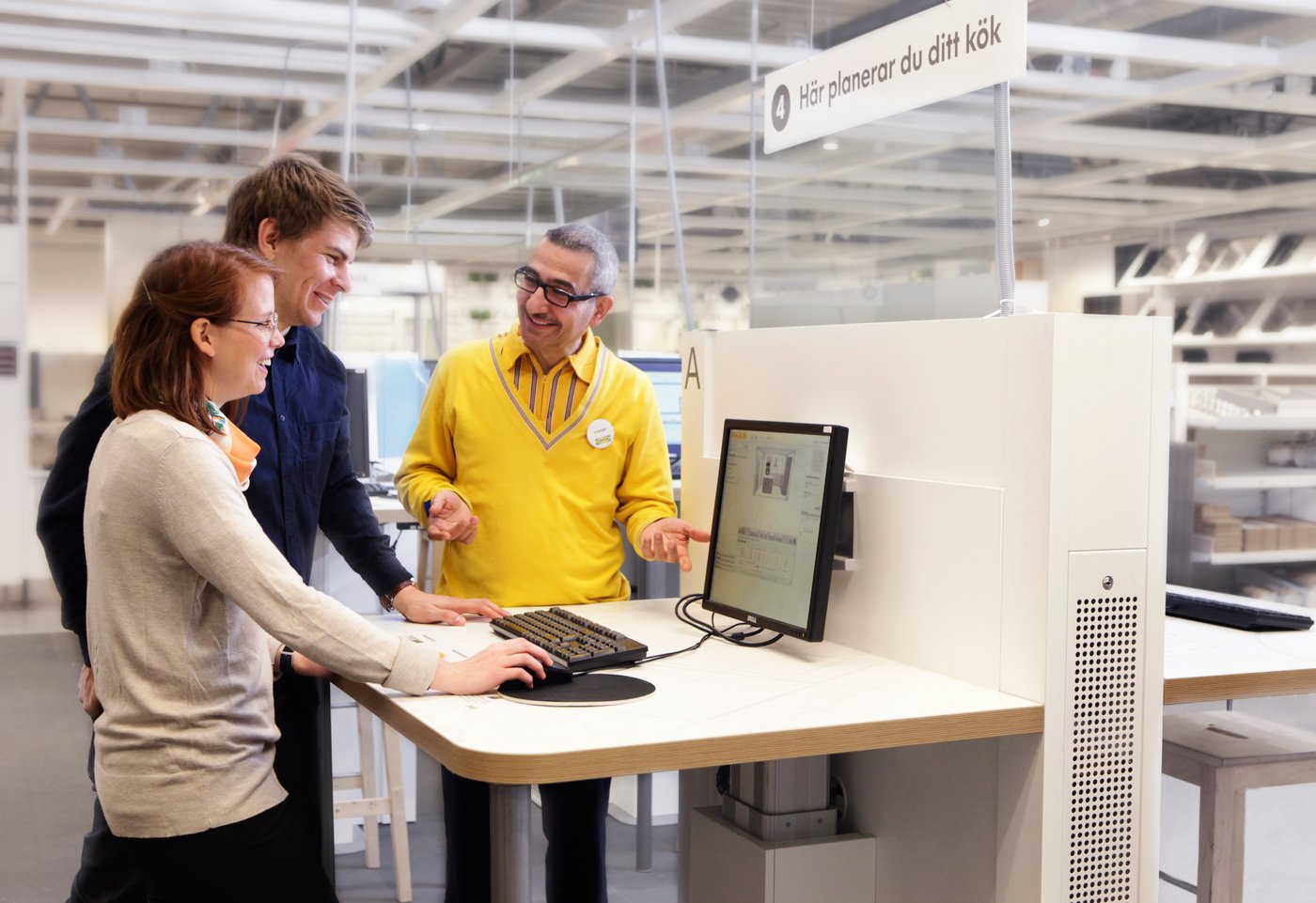En IKEA medarbetare står och hjälper två kunder att planera deras kök.