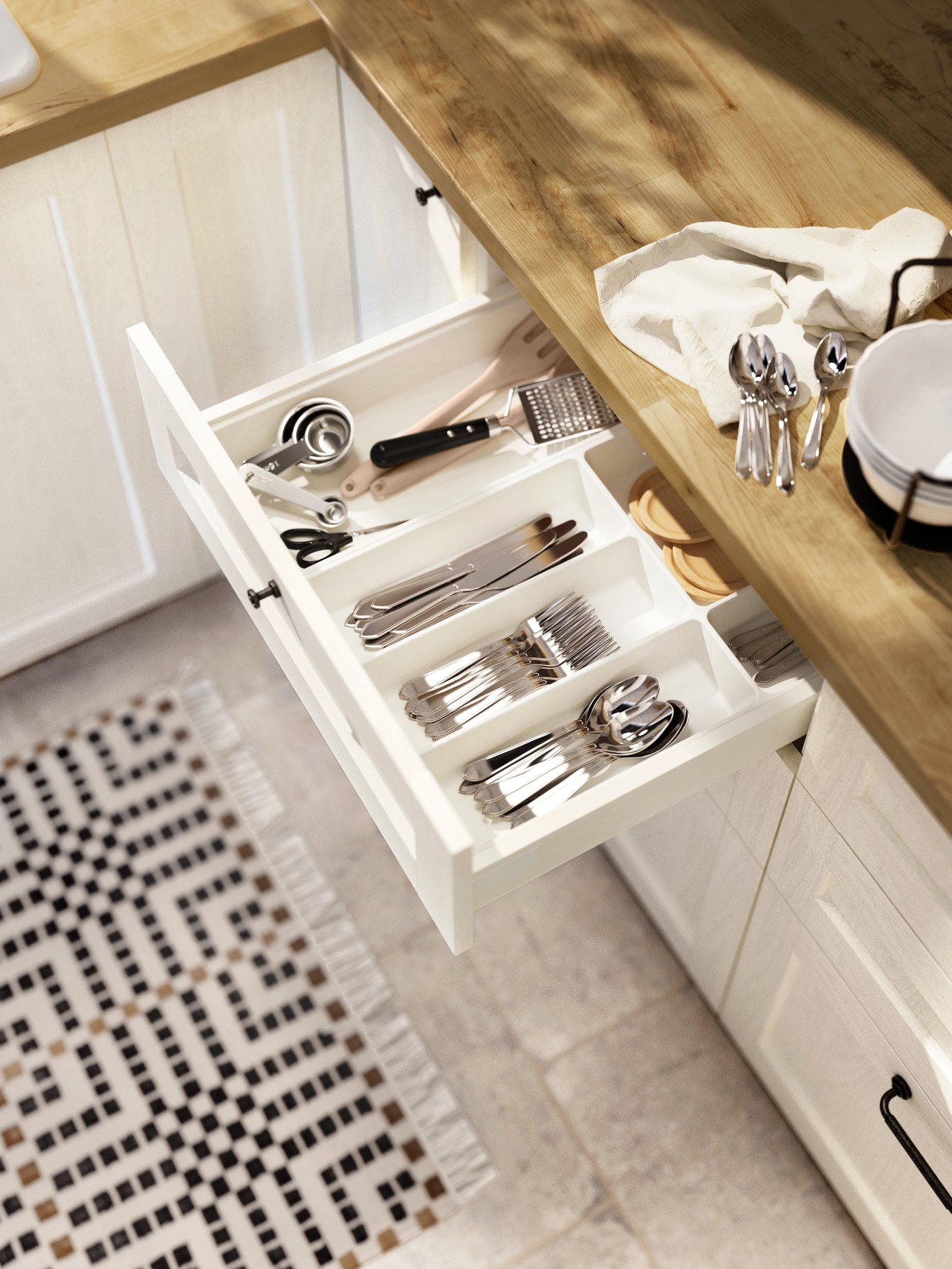 Una cocina con mesón de madera, un cajón del mueble de cocina está abierto mostrando un organizador de cubiertos con cucharas, cuchillos y tenedores.