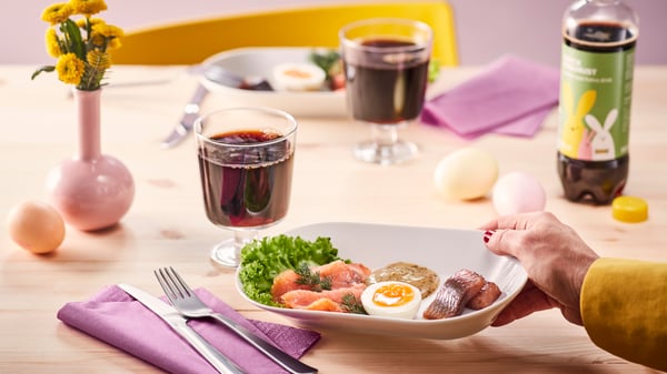 A birch wood table is lightly decorated for a swedish gathering. A plate of salmon and dill can be seen being place onto the spring table