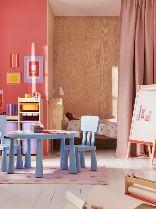 A light blue MAMMUT children’s table and two chairs on a pink BARNDÖM rug in a colourful children’s room.