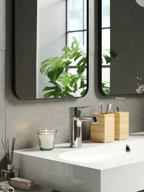 Plan de salle de bains avec accent sur un distributeur de savon beige en bambou, à côté d’un porte-brosses à dents beige et d’une bougie parfumée en verre. 