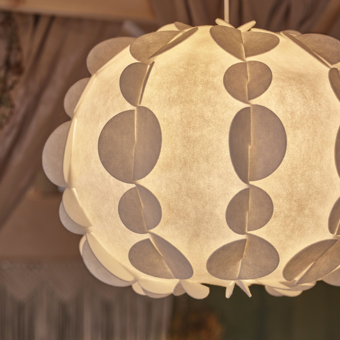 Ze stropu v místnosti se zelenými stěnami visí bílé stínidlo závěsné lampy PEKTOLIT s rozsvícenou žárovkou.