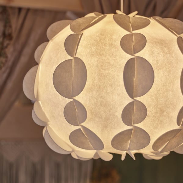 A white PEKTOLIT pendant lampshade, which has a lit light bulb inside it, hangs from a ceiling in a room with green walls.