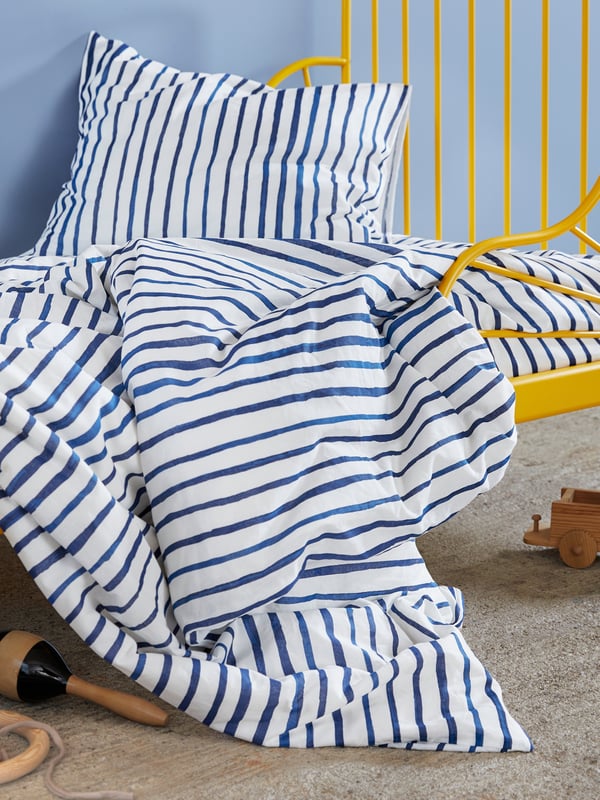 A bed with a white/blue striped SMALFRÄKEN quilt cover and pillowcase.