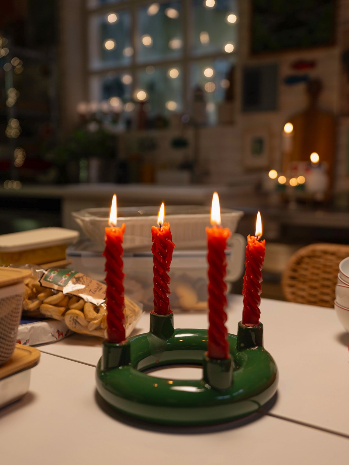 Primo piano del portacandele VINTERFINT verde con quattro candele rosse accese, che crea un'atmosfera di festa su un tavolo.