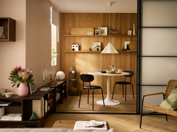 A warmly lit, spacious living room with a white round DOCKSTA table and two black ÖSTANÖ chairs, and a white ZEBRASÄV lamp.