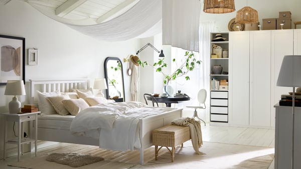 A white HEMNES double bed in a bright airy white bedroom with a black INGATORP extendable table by a window behind it.