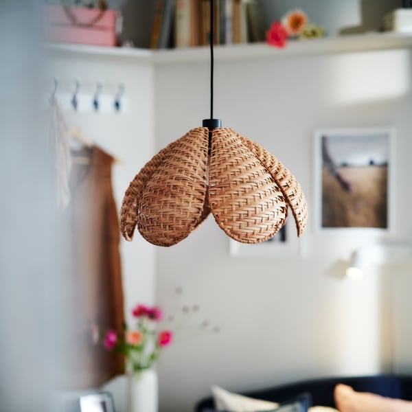 Ett ljust rum med väggar prydda med kläder, affischer och en hög hylla, samt en SANDKORN rottingpendellampa i mitten.
