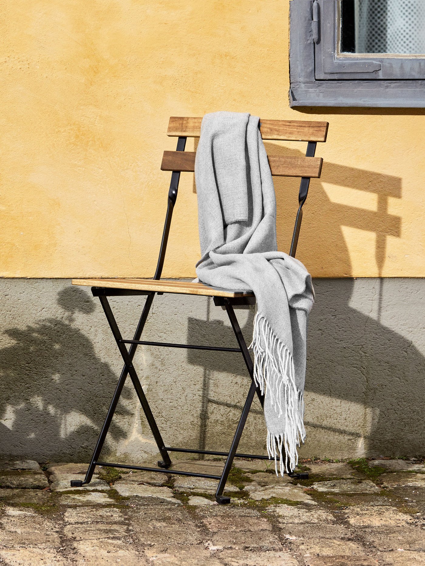 Una silla de terraza plegable TÄRNÖ apoyada en una pared.