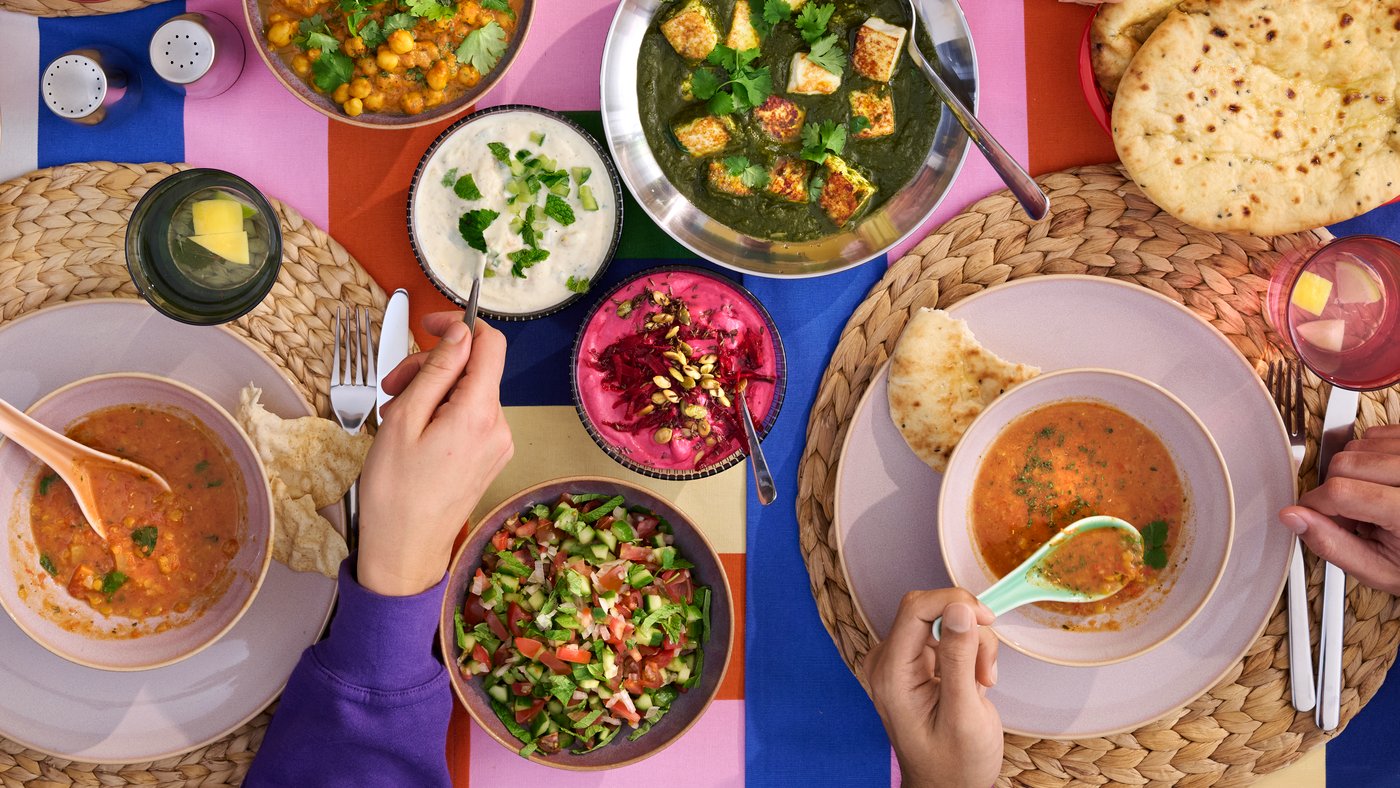 Folk forsyner sig med forskellige farverige retter, der er placeret på en dug med et sjovt, stribet mønster.