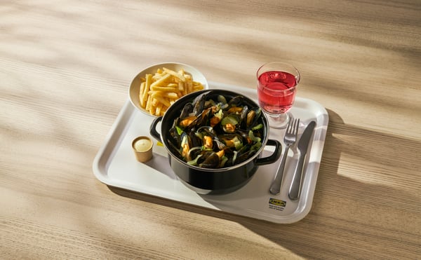 Mosselen met frietjes en saus, geserveerd op een IKEA dienblad met glas roze drank en bestek op houten tafel.