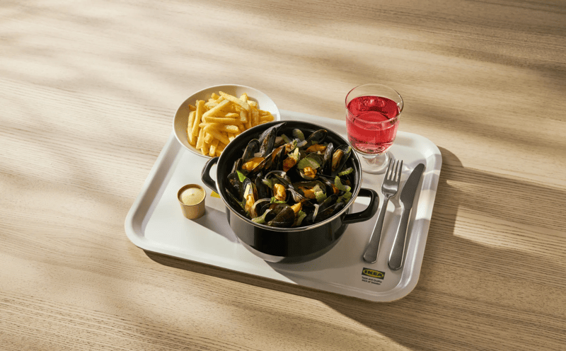Mosselen met frietjes en saus, geserveerd op een IKEA dienblad met glas roze drank en bestek op houten tafel.