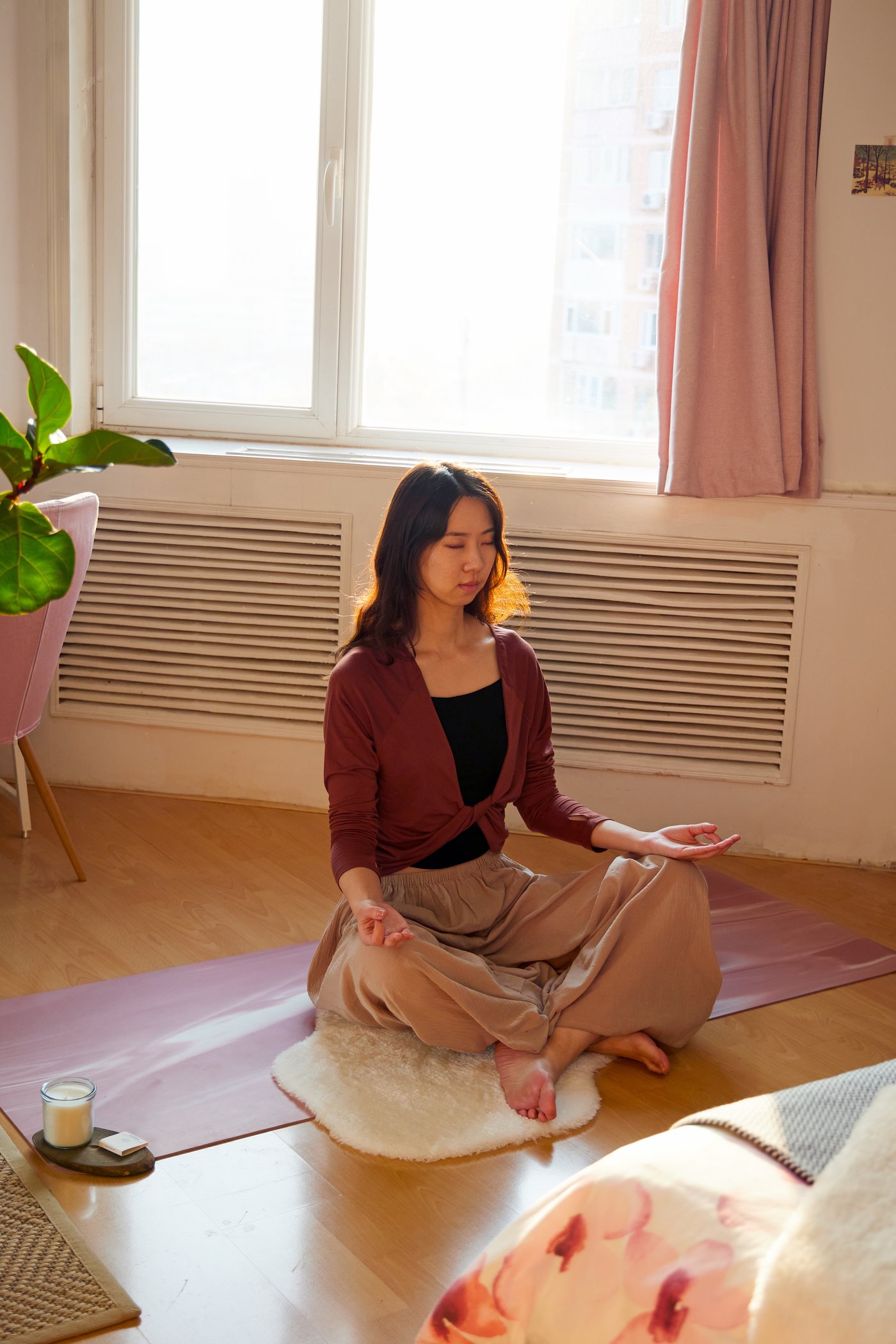 Woman meditating on the floor in her room next to a window, with soft white TOFTLUND rug used for support.