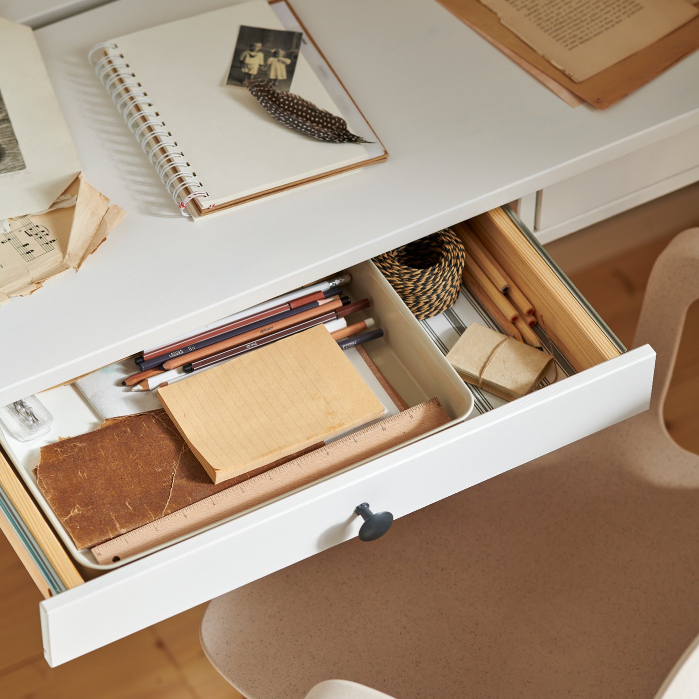 A white stain HEMNES desk with two drawers, with one drawer open with a plastic/beige organiser and stationery inside.