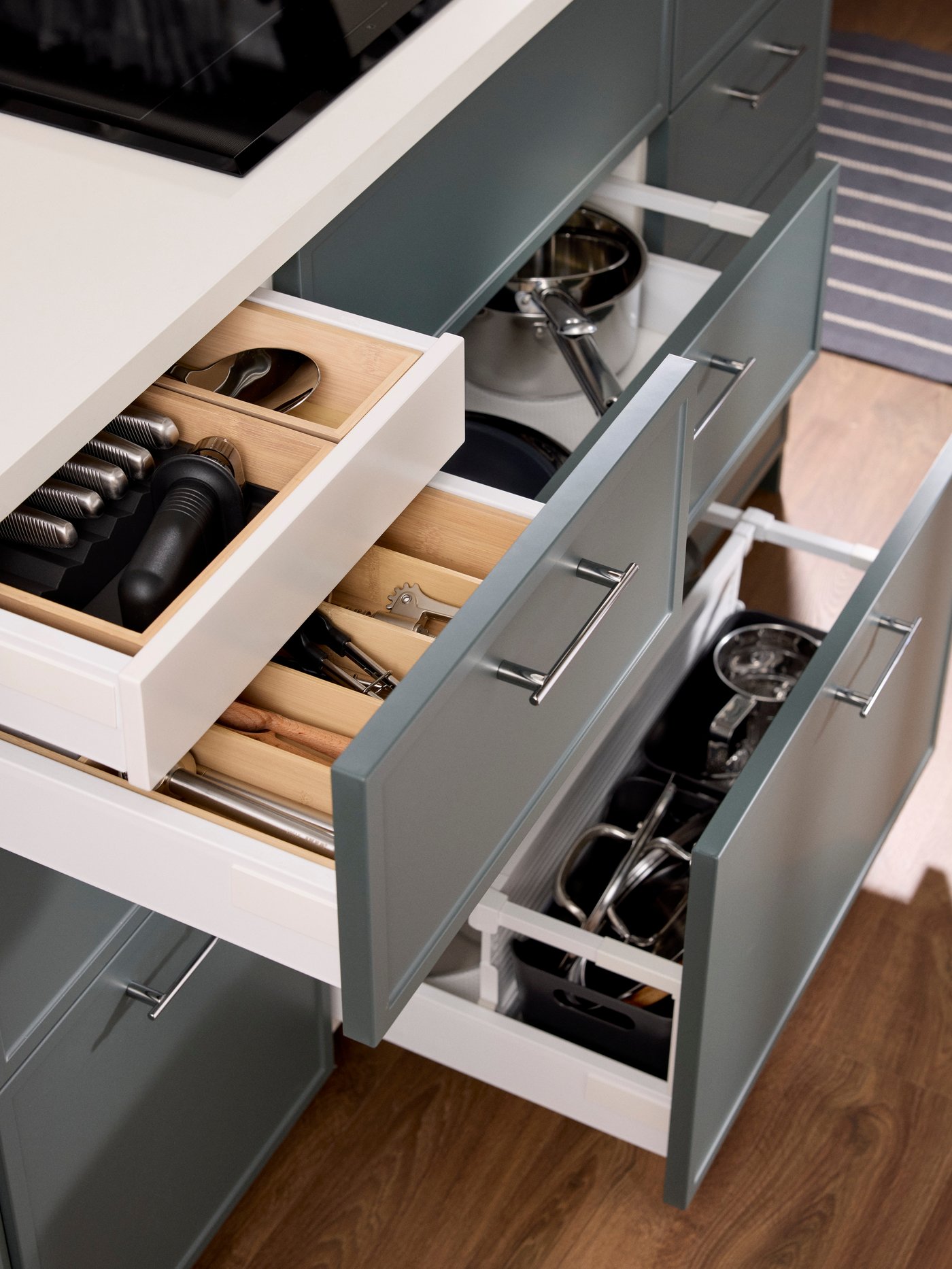 Kitchen drawers with dark grey-green ASPUDDEN fronts open to show bamboo organisers inside filled with kitchen utensils.