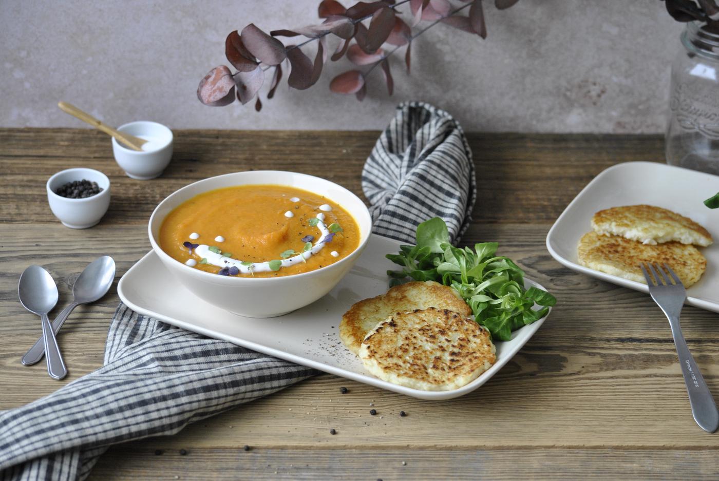 Soupe crémeuse à l'orange garnie d'herbes, servie avec une salade et du pain croustillant sur une table rustique en bois.