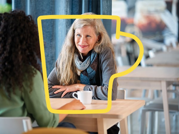 En smilende kvinde med langt hår nyder en kaffe i en IKEA-restaurant med en kvinde med langt krøllet hår.