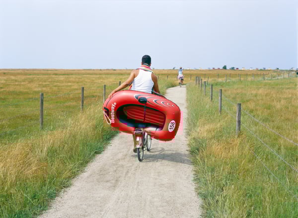 Un chico en bici por un camino de tierra con una colchoneta inflable