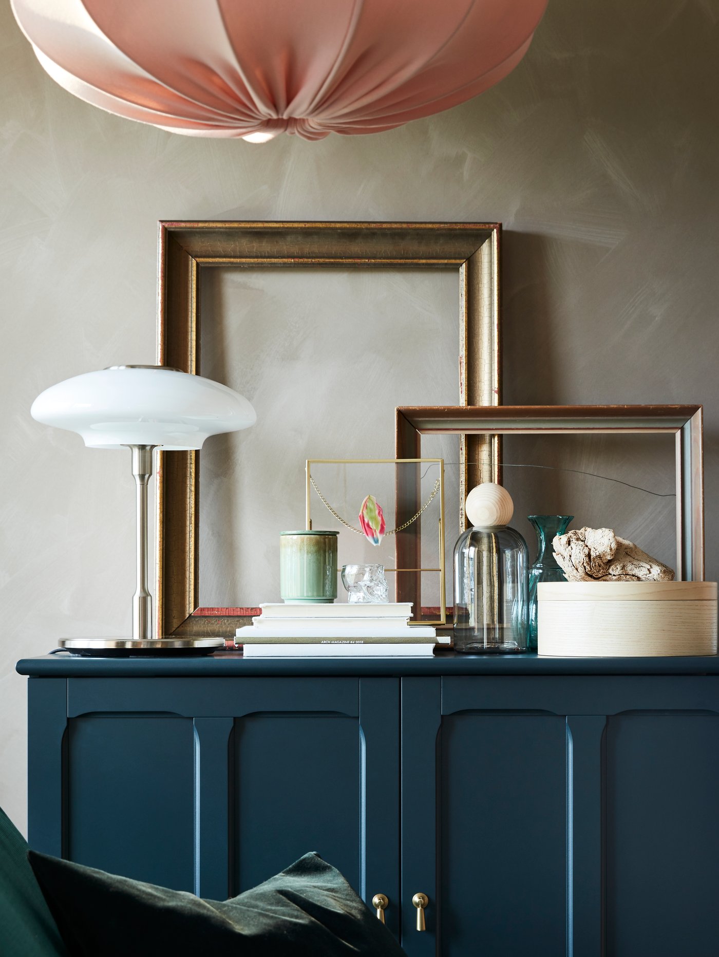 Golden frames, books, decorative items and a table lamp in nickel-plated/opal white glass stand on a blue-green cabinet.
