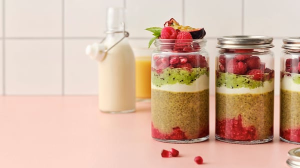 Chia pudding, red berries, yoghurt and kiwi are layered in a glass jar with a slice of passion fruit and mint leaves on top.