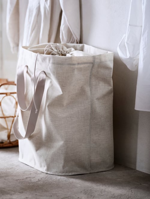 A modern laundry room featuring a beige laundry bag with a smaller bag and clothing items inside sitting on the floor. 