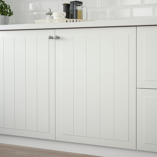 Køkkenskabe med STENSUND fronter i hvid med panel låger og knopper samt en hvid bordplade, hvor der står en bakke ovenpå.